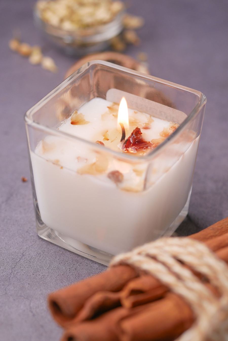 Weiße Duftkerze im Glas mit Zimtstangen
